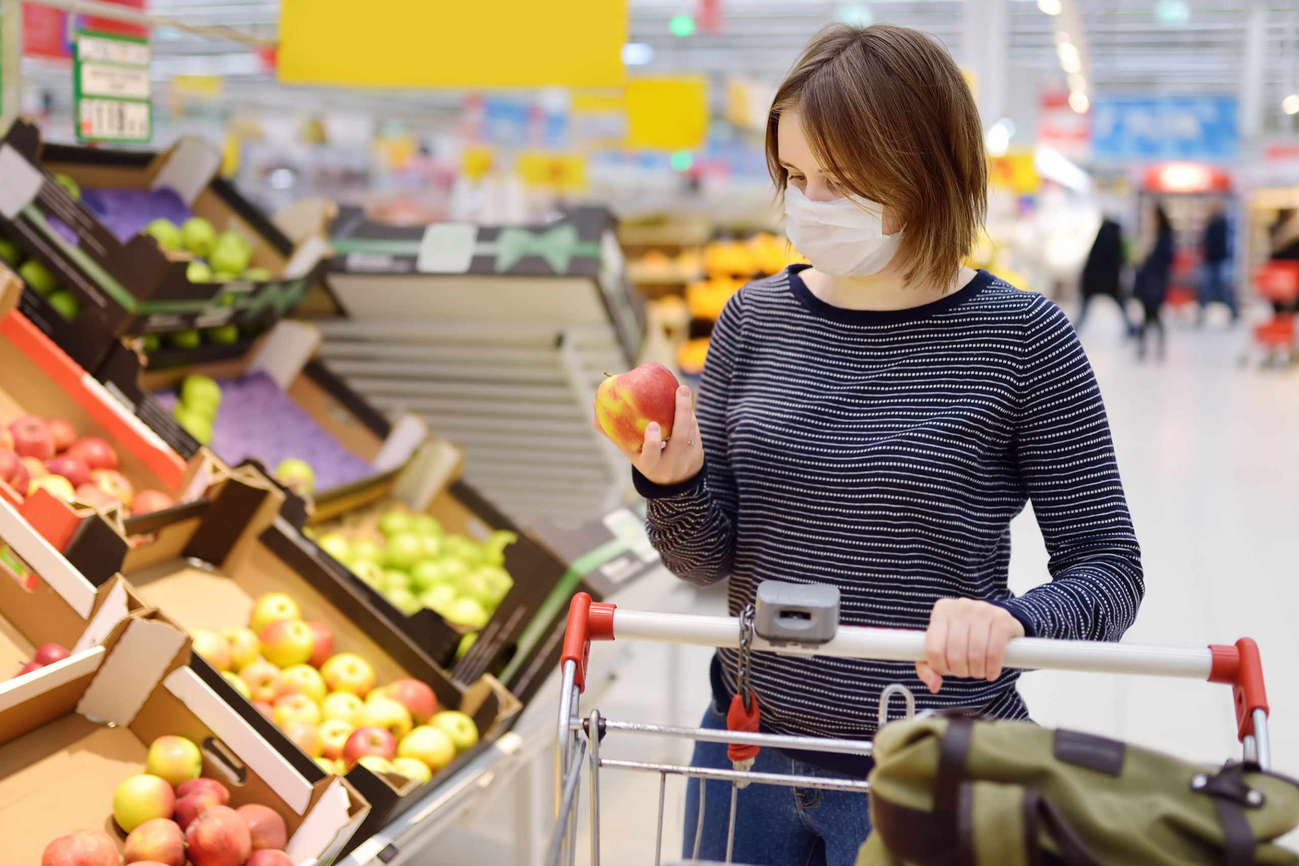 Ein Frau mit Maske betrachtet im Supermarkt einen Apfel. Symbolbild für die Debatte über die Inflation und die Krise.