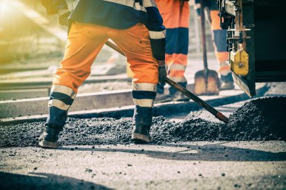 Straßenarbeiter in oranger Arbeitskleidung reißen eine asphaltierte Straße auf. Symbolbil für die Schwellenwert-Verordnung.