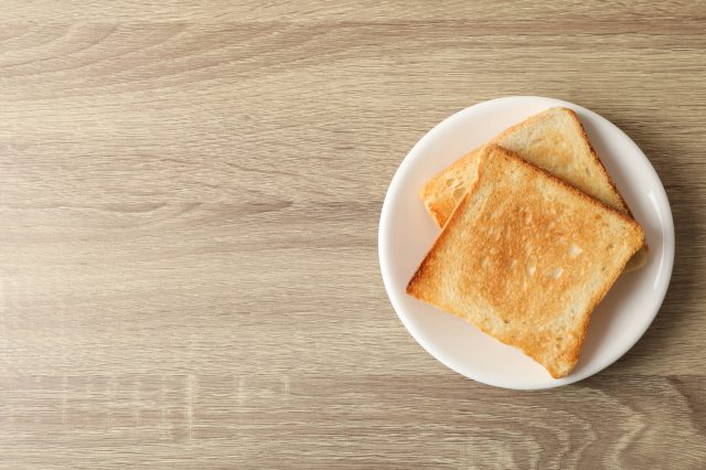 Zwei Scheiben Toastbrot liegen auf einem Teller, der auf einem Holztisch steht. Wer in Armut lebt kennt Toastbrottage.