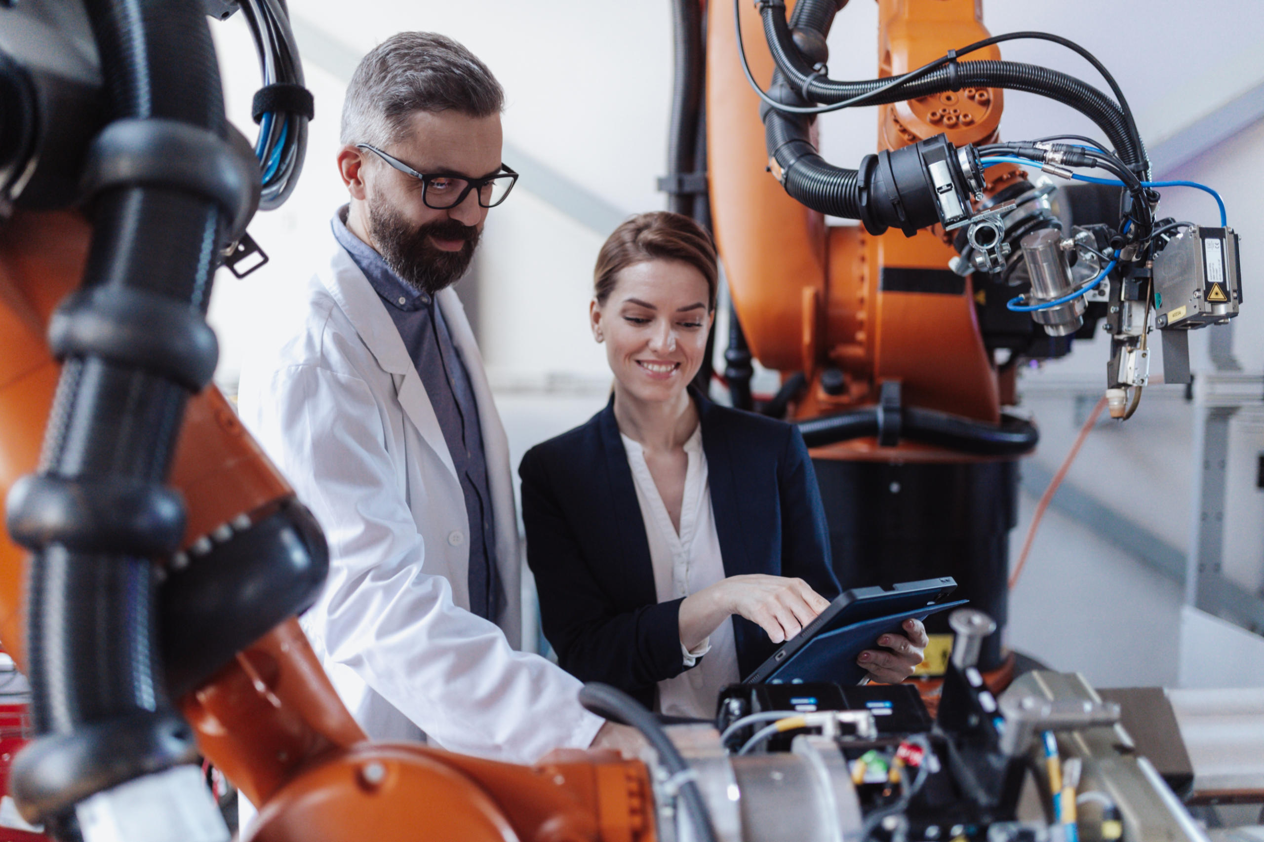 In der Fabrik eines Industrieunternehmens unterhalten sich zwei Beschäftigte vor einem Robotor über Digitalisierung.