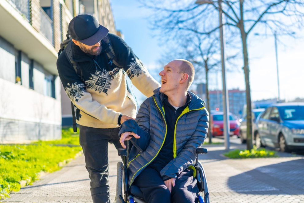 Ein Mann im Rollstuhl scherzt mit einer Person aus der Pflege.