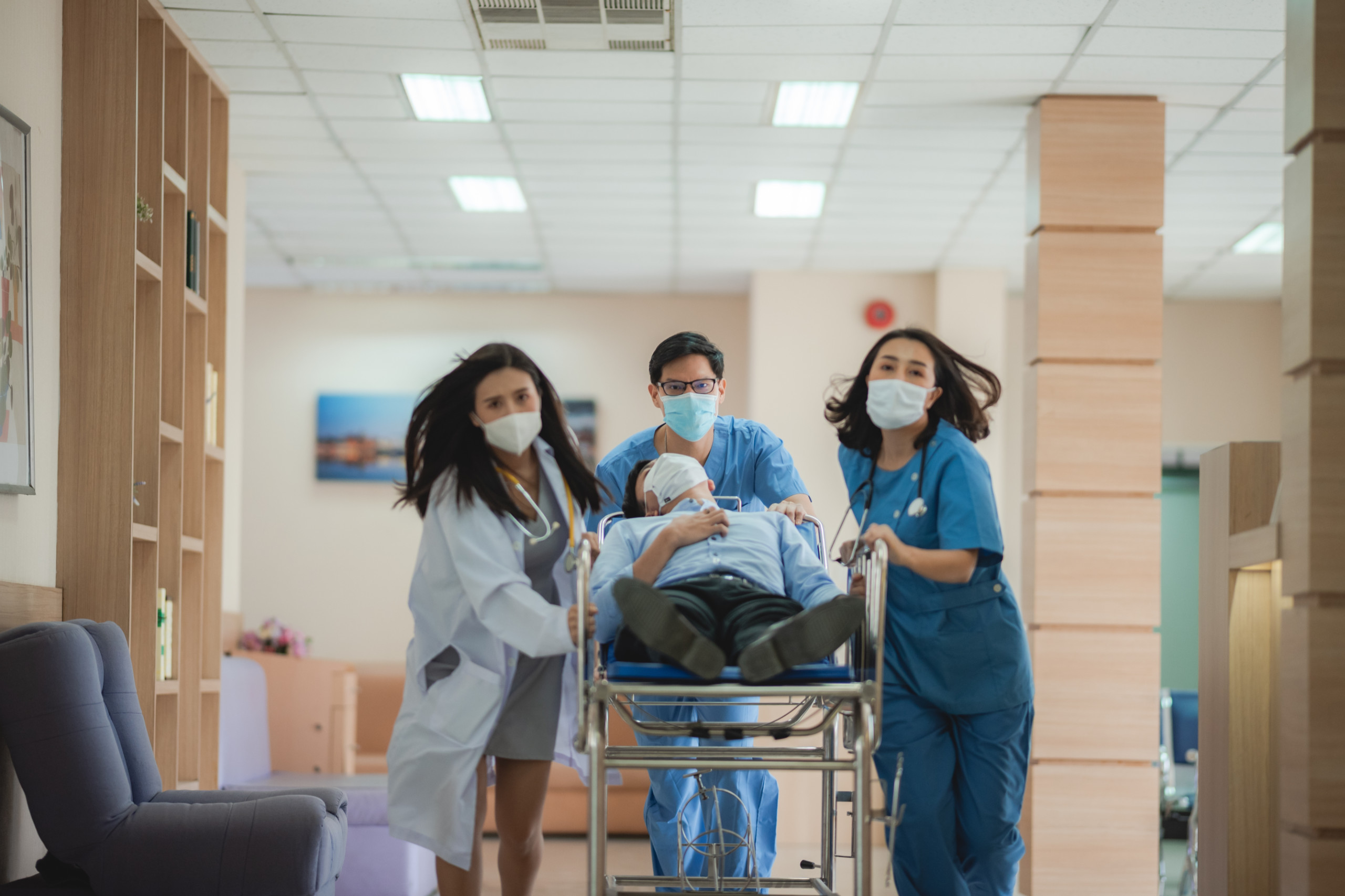 Ein gestresstes team schiebt ein Bett durch einen Flur im Krankenhaus. Die Pflegekrise und der Pflegenotstand stresst das Personal.