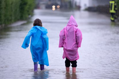 Zwei Kinder in Regenmantel stehen im Hochwasser.