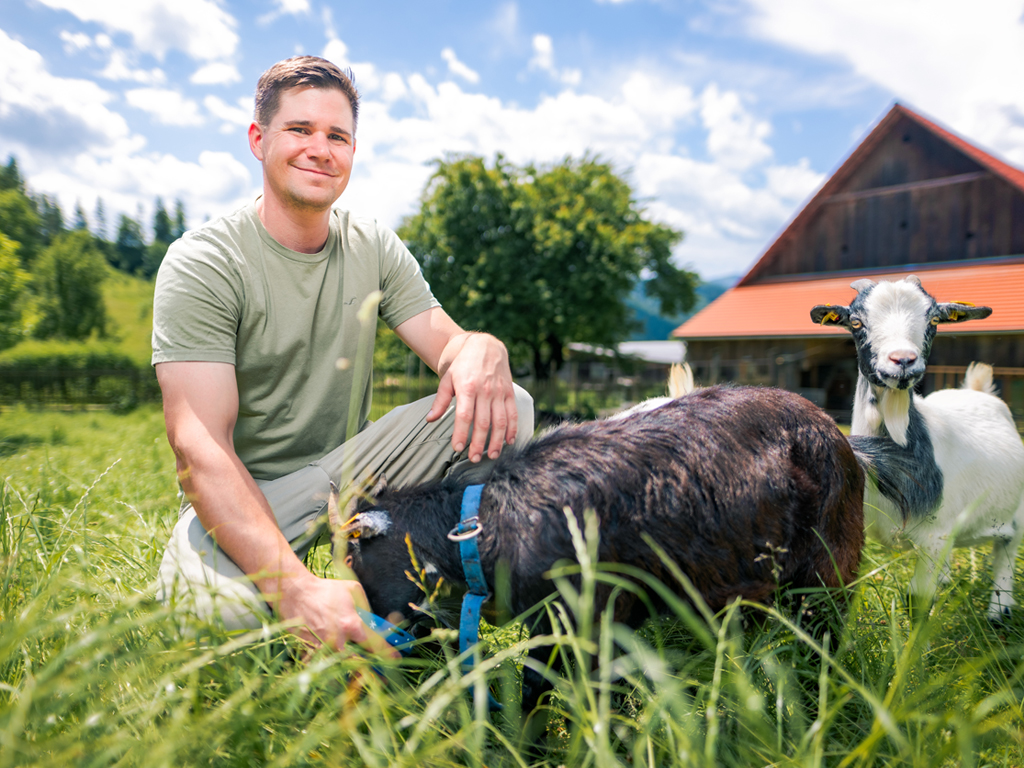 Porträt Stefan Schwaighofer. Er sitzt hinter zwei Ziegen. 