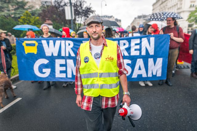 Gregor Stöhr auf einer Demo. Hinter ihm stehen Demonstrant:innen, die ein Schild mit der Aufschrift "Wir fahren gemeinsam" halten.