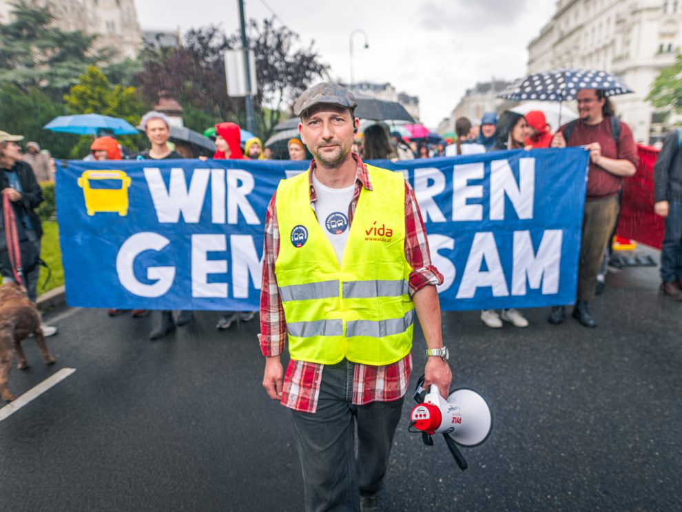 Gregor Stöhr auf einer Demo. Hinter ihm stehen Demonstrant:innen, die ein Schild mit der Aufschrift "Wir fahren gemeinsam" halten.