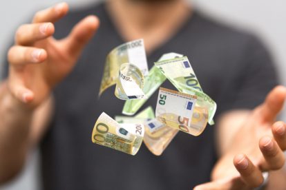 Zwischen den Händen eines Mannes schweben Geldscheine. Symbolbild über gekürzte Lohnnebenkosten.