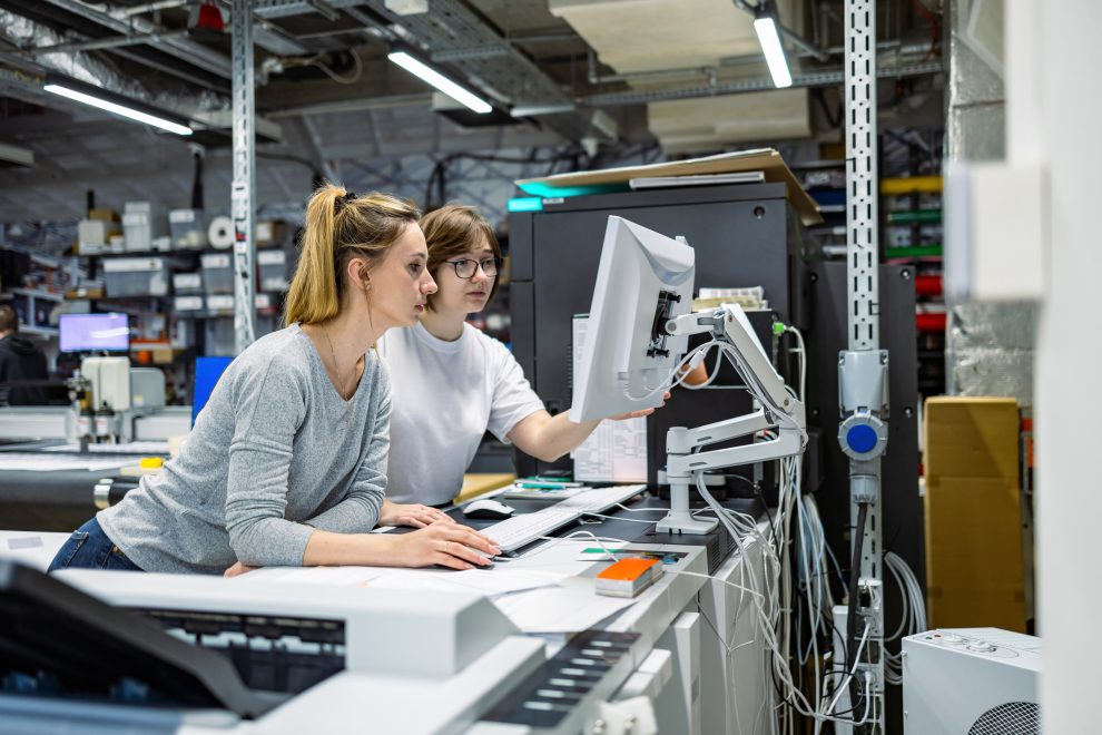 Zwei Frauen stehen an einem Computer. Sie arbeiten in der Druckindustrie. Symbolbild für die Industrie.