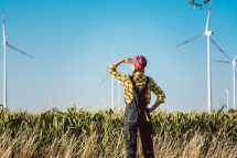 Eine Landwirtin steht vor ihrem Maisfeld mit Windrädern. Just Transition soll das Soziale ins Ökologische bringen.