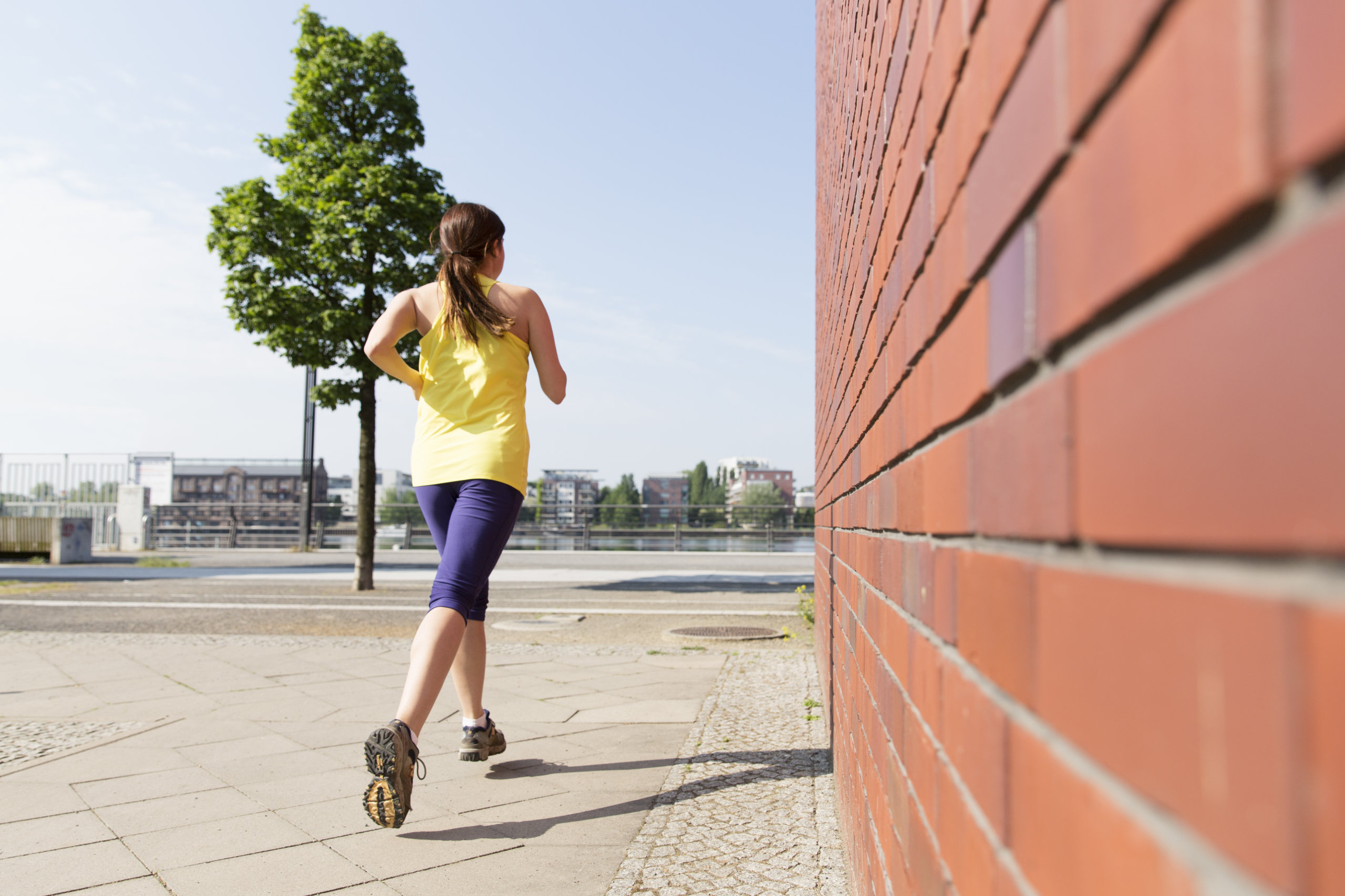 Eine Frau joggt an einer Mauer aus Ziegeln der Firma Wienerberger vorbei. 