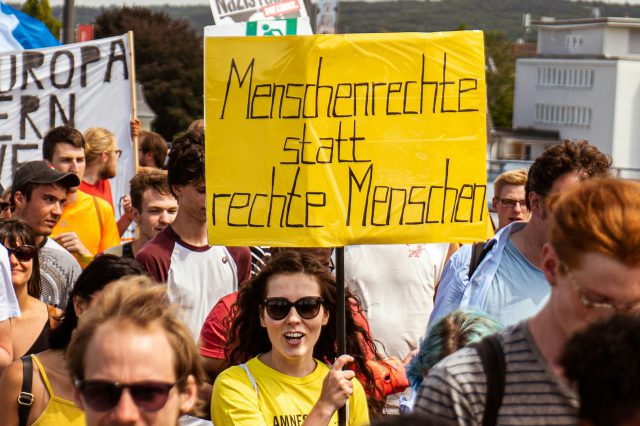 Eine Demonstration gegen Rechts. Eine Frau steht im Vordergrund und hält ein Schild mit der Aufschrift "Menschenrechte statt rechte Menschen". Daniela Ingruber erklärt im Interview den Erfolg rechter Populisten.