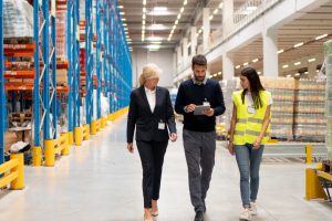 Drei Menschen besichtigen die Lagerhalle einer Fabrik.