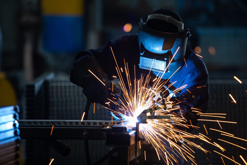 Arbeiter in Industriekleidung und mit geschweißter Eisenmaske. Symbolbild für die Prognose der Wirtschaft 2025.