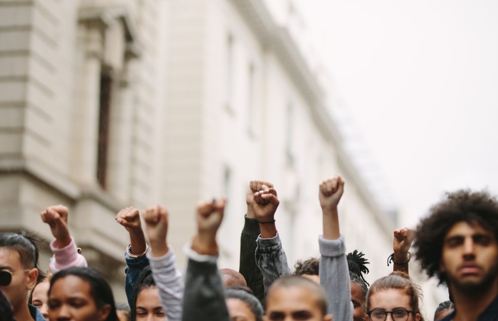 Menschen in einem Protest, strecken ihre Hände hoch, um sich für Demokratie einzusetzen.