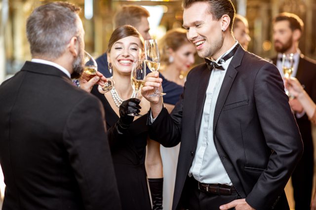 Menschen in Abendkleidung prosten sich mit Champagnergläsern zu. Symbolbild für Superreiche.